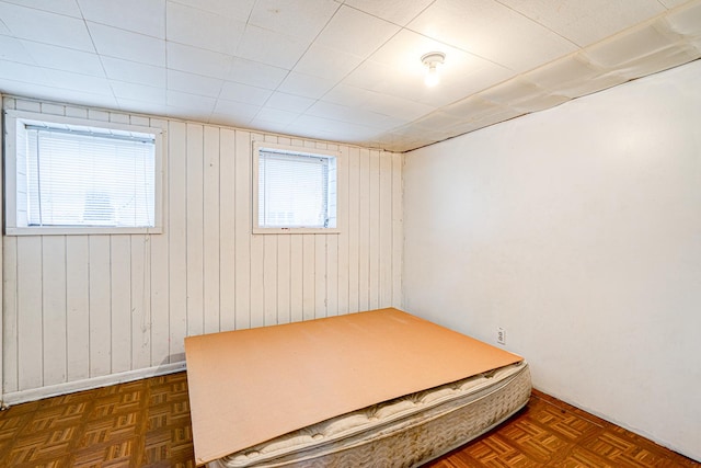 unfurnished bedroom featuring dark parquet floors, multiple windows, and wooden walls