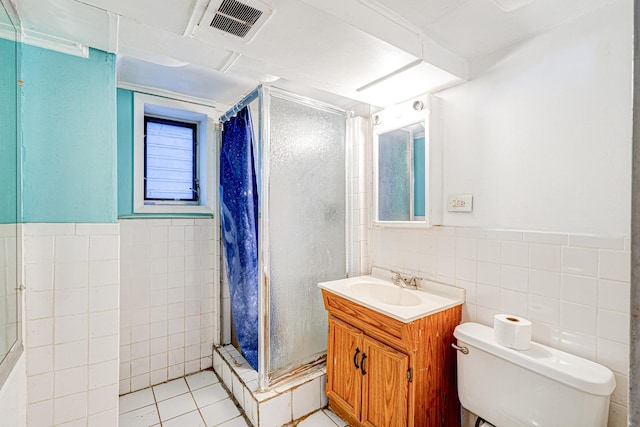 bathroom with vanity, tiled shower, tile walls, tile patterned flooring, and toilet