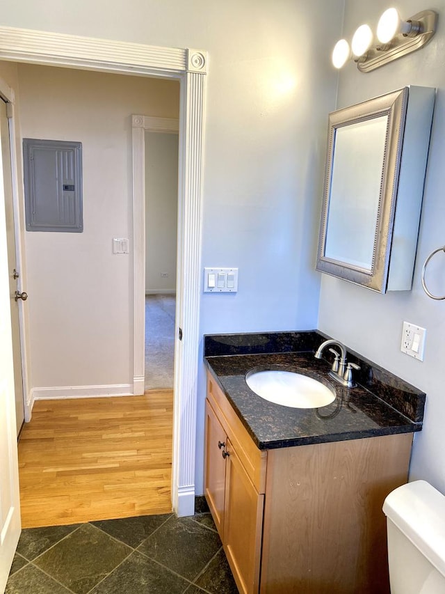 bathroom featuring vanity, electric panel, hardwood / wood-style flooring, and toilet