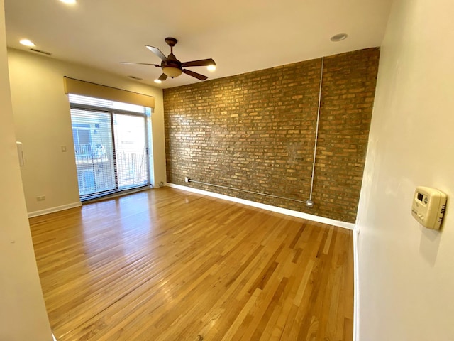 empty room featuring light hardwood / wood-style floors, ceiling fan, and brick wall