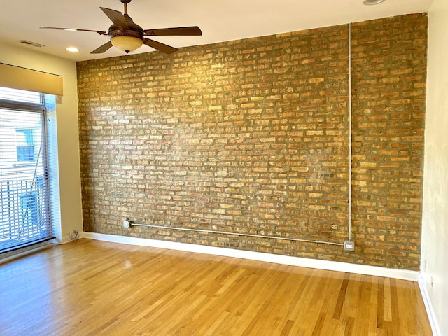 spare room featuring ceiling fan, hardwood / wood-style floors, and brick wall