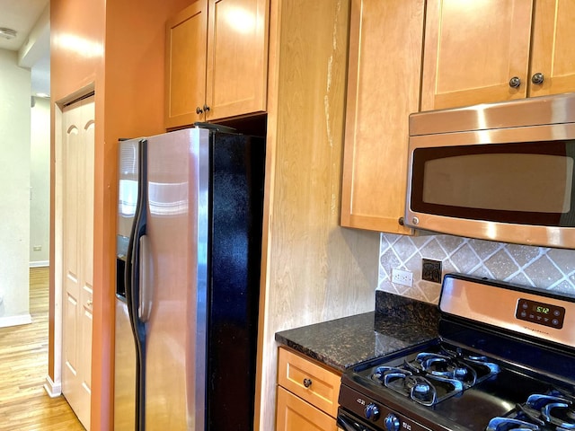 kitchen featuring backsplash, light hardwood / wood-style floors, dark stone counters, and appliances with stainless steel finishes