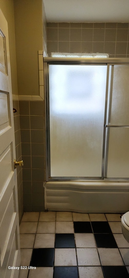 bathroom with tile patterned floors, shower / bath combination with glass door, and toilet