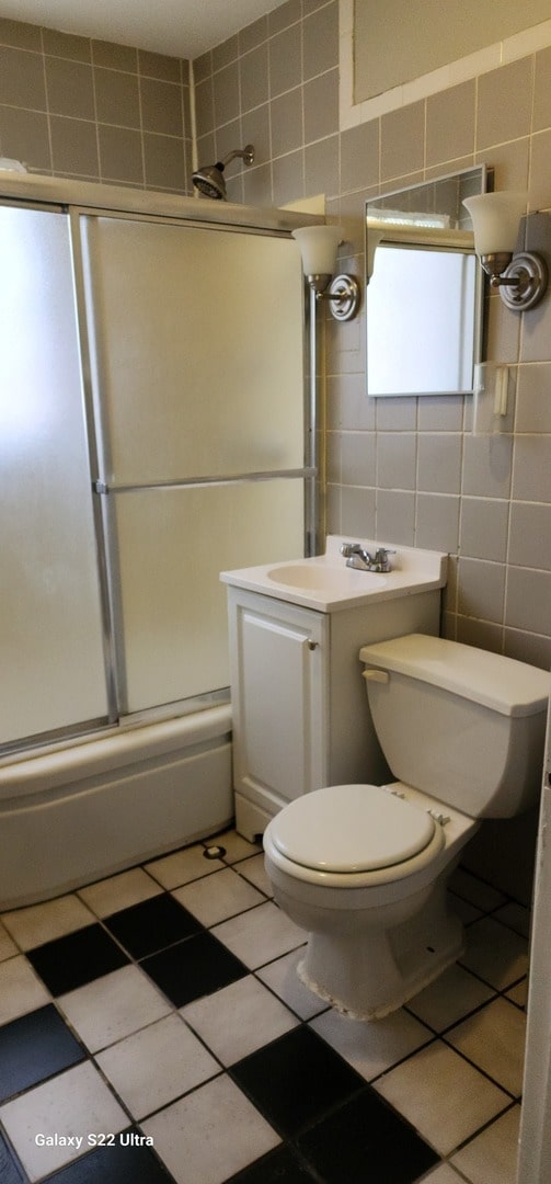 full bathroom featuring shower / bath combination with glass door, vanity, tile walls, and toilet