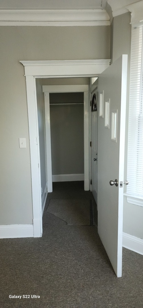 hallway with dark carpet and crown molding