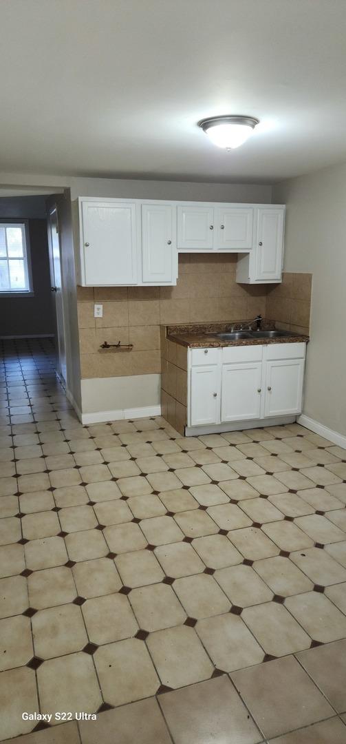 8350 S Muskegon Ave, Chicago, IL 60617 - kitchen featuring a sink, white cabinets, dark countertops, baseboards, and decorative backsplash