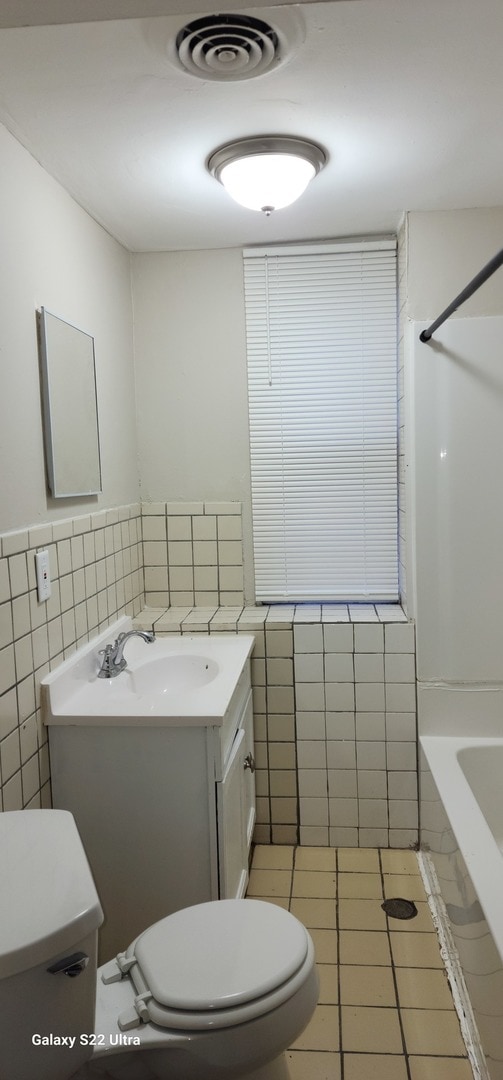 bathroom featuring toilet, vanity, tile patterned floors, and tile walls