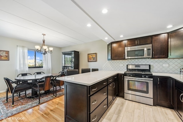 kitchen featuring a notable chandelier, kitchen peninsula, light hardwood / wood-style floors, decorative light fixtures, and appliances with stainless steel finishes