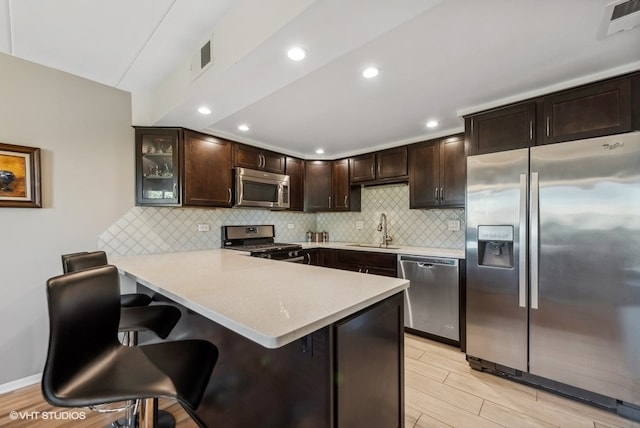 kitchen featuring kitchen peninsula, appliances with stainless steel finishes, decorative backsplash, a kitchen breakfast bar, and sink