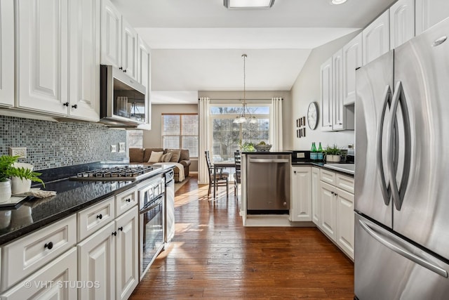 kitchen with stainless steel appliances, lofted ceiling, dark stone counters, pendant lighting, and white cabinets