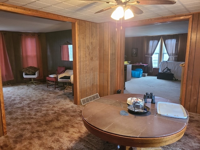 dining room with wood walls, carpet, and ceiling fan