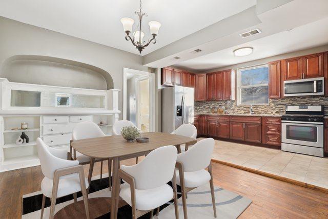 kitchen with hanging light fixtures, an inviting chandelier, light hardwood / wood-style floors, decorative backsplash, and appliances with stainless steel finishes