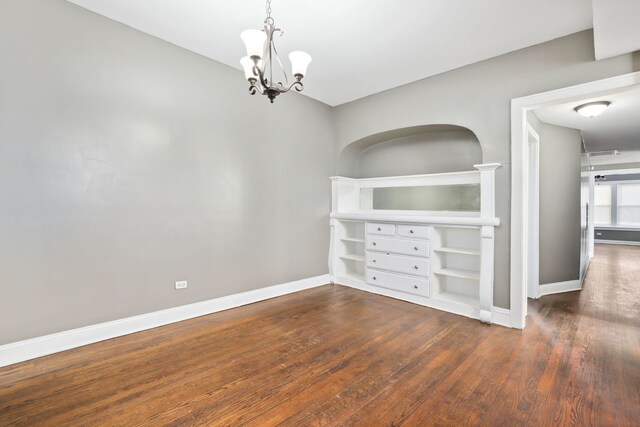 empty room with dark hardwood / wood-style flooring and an inviting chandelier