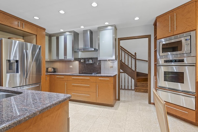 kitchen featuring stainless steel appliances, tasteful backsplash, dark stone countertops, and wall chimney range hood