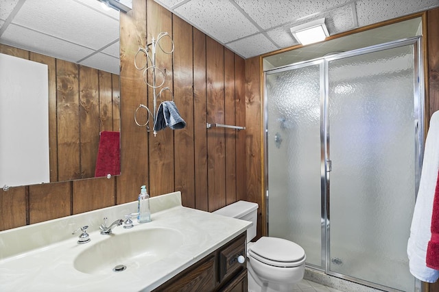 bathroom featuring a paneled ceiling, vanity, a shower with door, wooden walls, and toilet