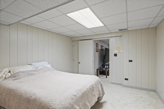 carpeted bedroom with a paneled ceiling and wood walls