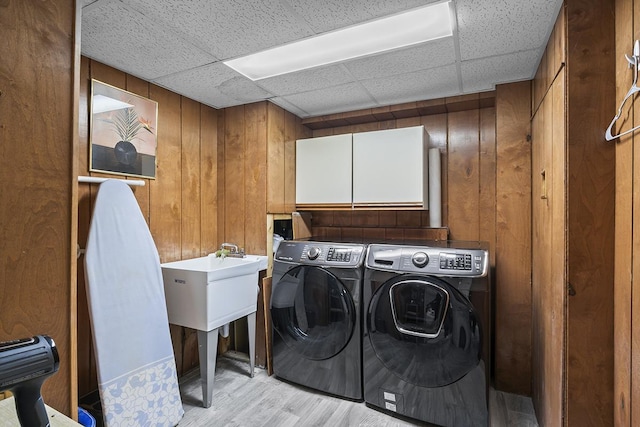 laundry area featuring cabinets, independent washer and dryer, light hardwood / wood-style floors, and wood walls