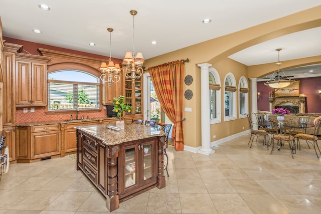 kitchen featuring light stone countertops, a center island, sink, tasteful backsplash, and decorative columns