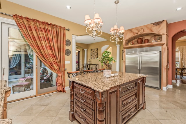 kitchen with a center island, built in fridge, hanging light fixtures, ornate columns, and a chandelier