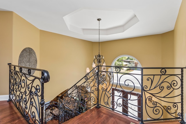 staircase featuring a raised ceiling, wood-type flooring, and an inviting chandelier