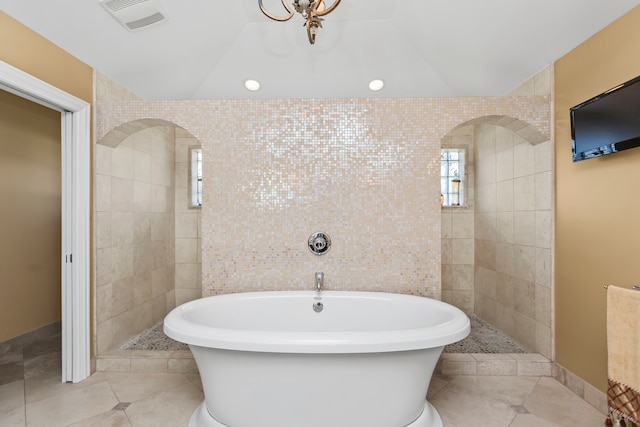 bathroom with tile patterned flooring, a bathtub, lofted ceiling, and tile walls