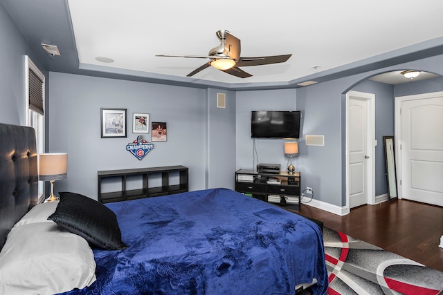 bedroom with ceiling fan, dark hardwood / wood-style floors, and a tray ceiling