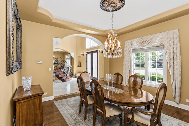 dining space with a notable chandelier, a raised ceiling, dark wood-type flooring, and french doors