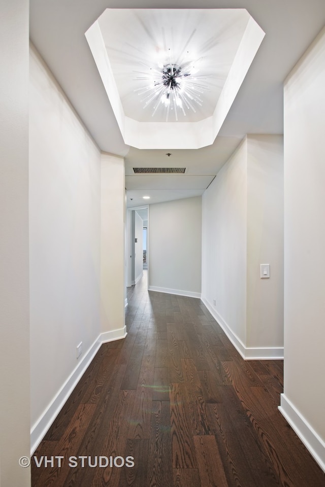 hallway with a tray ceiling, an inviting chandelier, and dark wood-type flooring