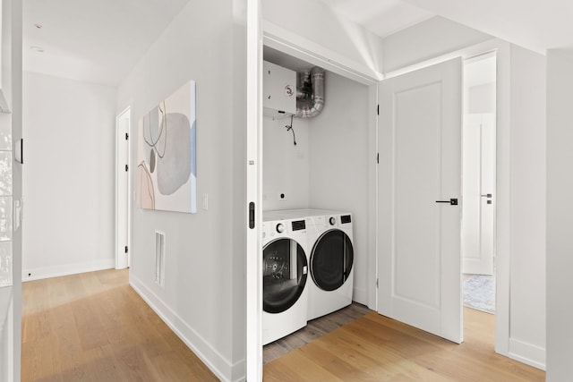 clothes washing area with light wood-type flooring, washing machine and dryer, and water heater