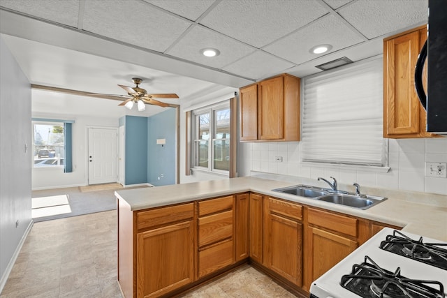 kitchen featuring kitchen peninsula, tasteful backsplash, gas range gas stove, ceiling fan, and sink