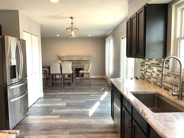 kitchen featuring dark wood-type flooring, sink, hanging light fixtures, light stone counters, and stainless steel appliances