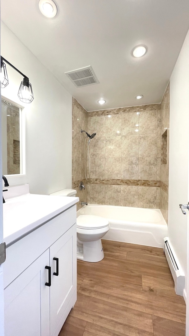 full bathroom featuring vanity, baseboard heating, wood-type flooring, toilet, and tiled shower / bath