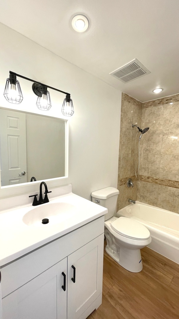 full bathroom with a baseboard radiator, tiled shower / bath combo, hardwood / wood-style floors, toilet, and vanity