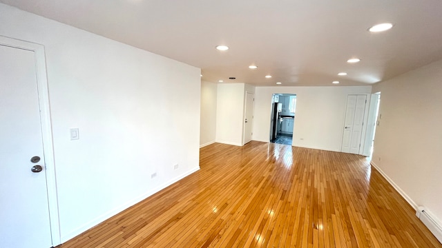 unfurnished room with light wood-type flooring, a baseboard radiator, and an AC wall unit