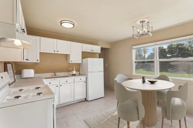 kitchen featuring white appliances, sink, light tile patterned floors, decorative light fixtures, and white cabinetry