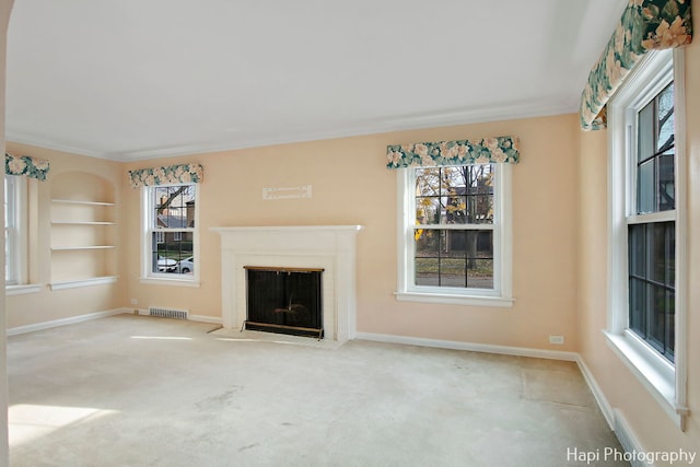 unfurnished living room featuring built in shelves, light colored carpet, and crown molding