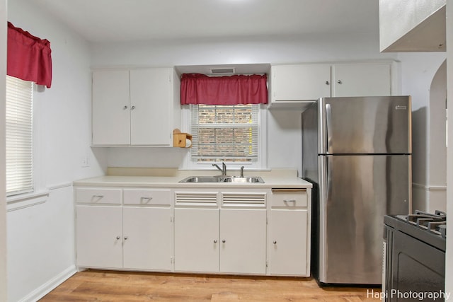 kitchen with white cabinets, light wood-type flooring, range, and sink