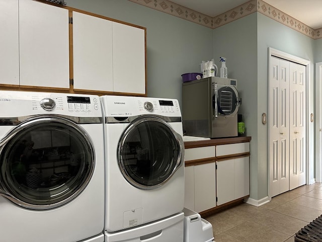 laundry room with washing machine and dryer, light tile patterned floors, and cabinets