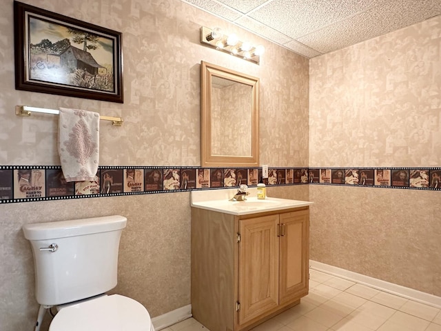 bathroom with tile patterned flooring, vanity, a drop ceiling, and toilet