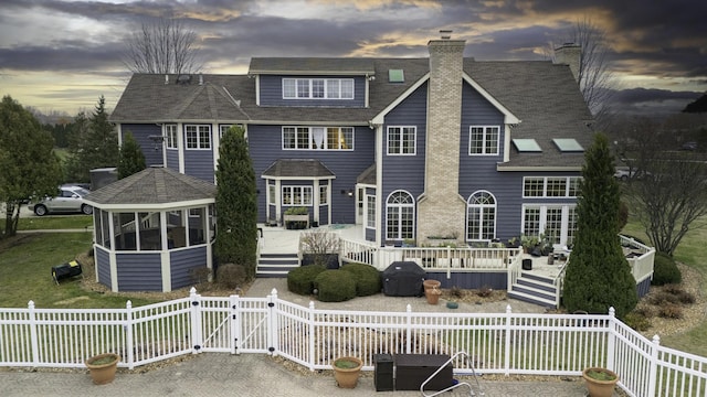 back house at dusk featuring a wooden deck and a sunroom