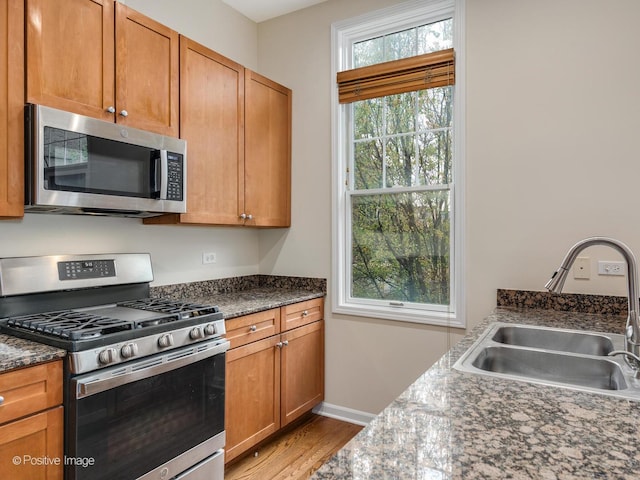 kitchen with appliances with stainless steel finishes, light hardwood / wood-style floors, dark stone countertops, and sink