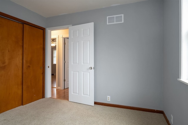 unfurnished bedroom with light colored carpet, multiple windows, and a closet