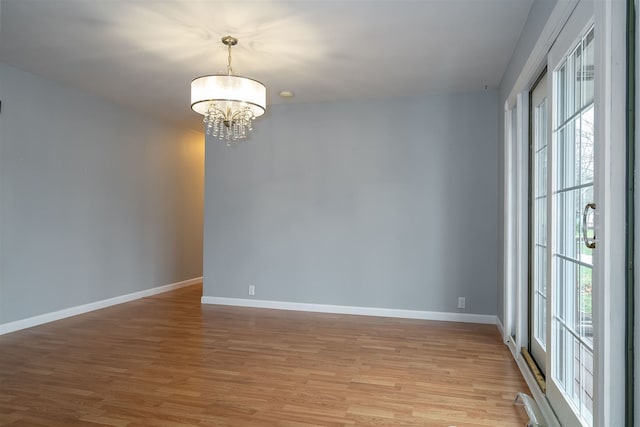 spare room featuring plenty of natural light, light hardwood / wood-style flooring, and a chandelier