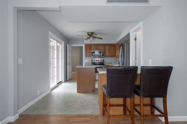 kitchen featuring a kitchen breakfast bar, stainless steel appliances, ceiling fan, sink, and light hardwood / wood-style flooring