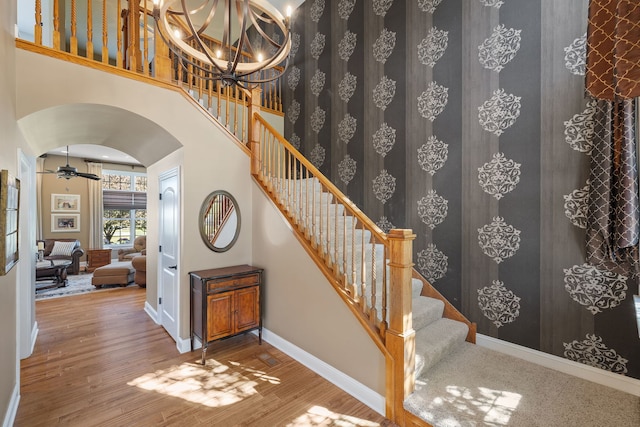 staircase with ceiling fan with notable chandelier, wood-type flooring, and a towering ceiling