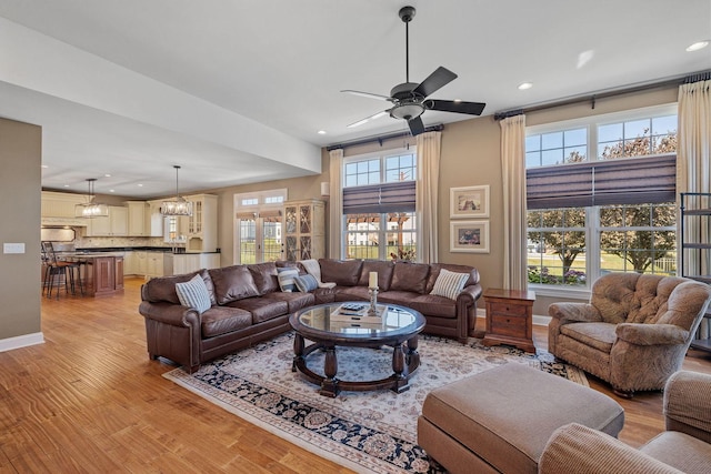 living room with ceiling fan with notable chandelier, light wood-type flooring, and a healthy amount of sunlight