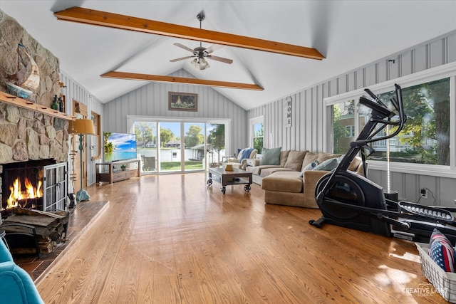 living room with ceiling fan, high vaulted ceiling, beamed ceiling, light hardwood / wood-style floors, and a stone fireplace