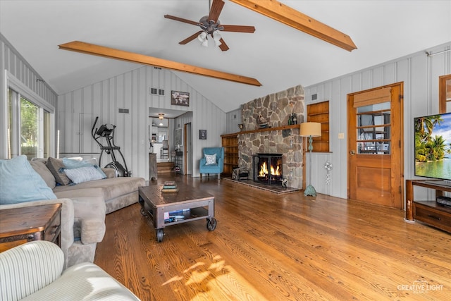 living room with hardwood / wood-style floors, vaulted ceiling with beams, a stone fireplace, and ceiling fan