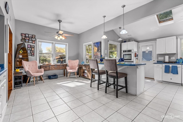 kitchen with ceiling fan, stainless steel oven, a breakfast bar, white cabinets, and vaulted ceiling with skylight