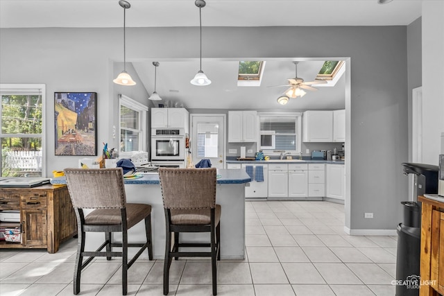 kitchen featuring white cabinetry, ceiling fan, double oven, lofted ceiling with skylight, and a breakfast bar